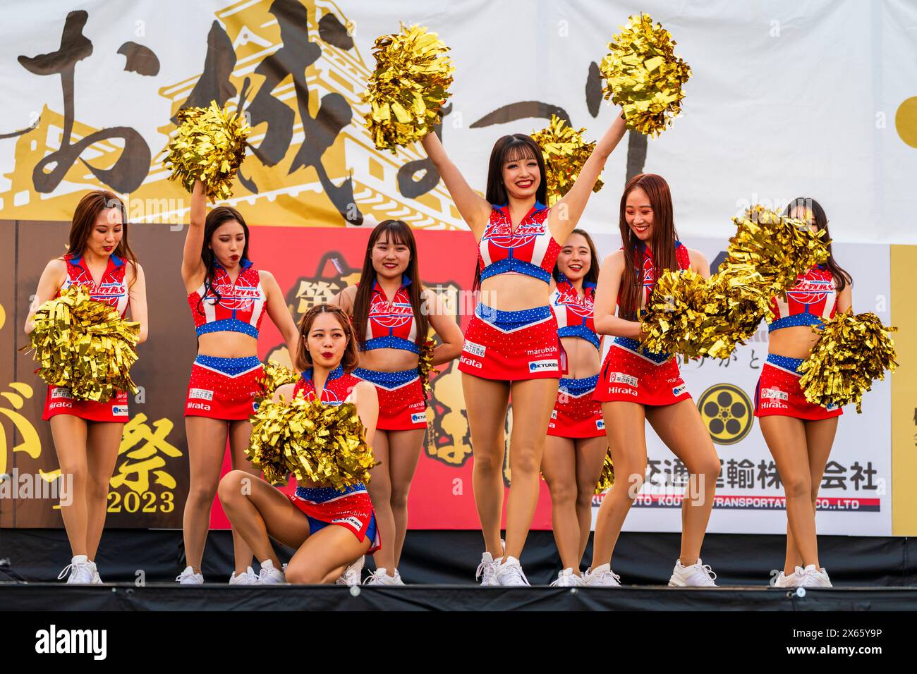 Japanese teenage women cheerleader Yosakoi dancers in tank tops and mini skirts dancing on stage holding gold glittery pom poms at the Kyusyu Gassai. Stock Photo