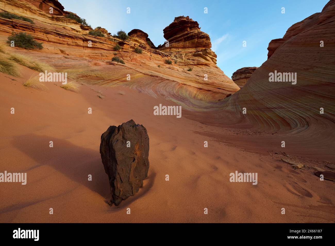 A lone rock in the sand in front of some wild rock formations in Stock Photo