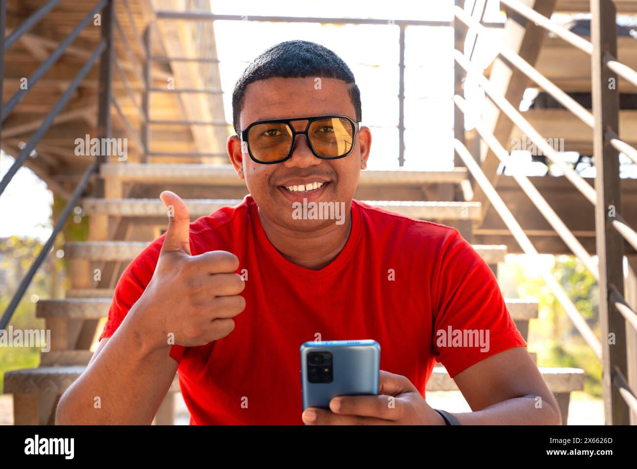 portrait smiling young black man pointing thumb up on blur background Stock Photo