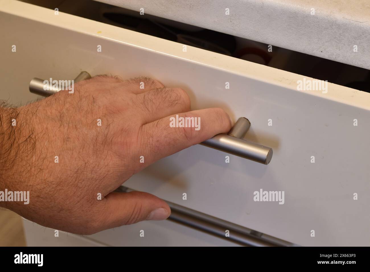 The photo shows a man's hand resting on the handle of a desk drawer. The man pulls out the desk drawer, grasping the metal handle. Stock Photo