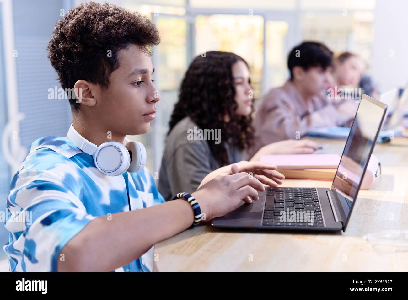 Side view portrait of Middle Eastern teenage boy using computer in library with diverse group of students in row copy space Stock Photo
