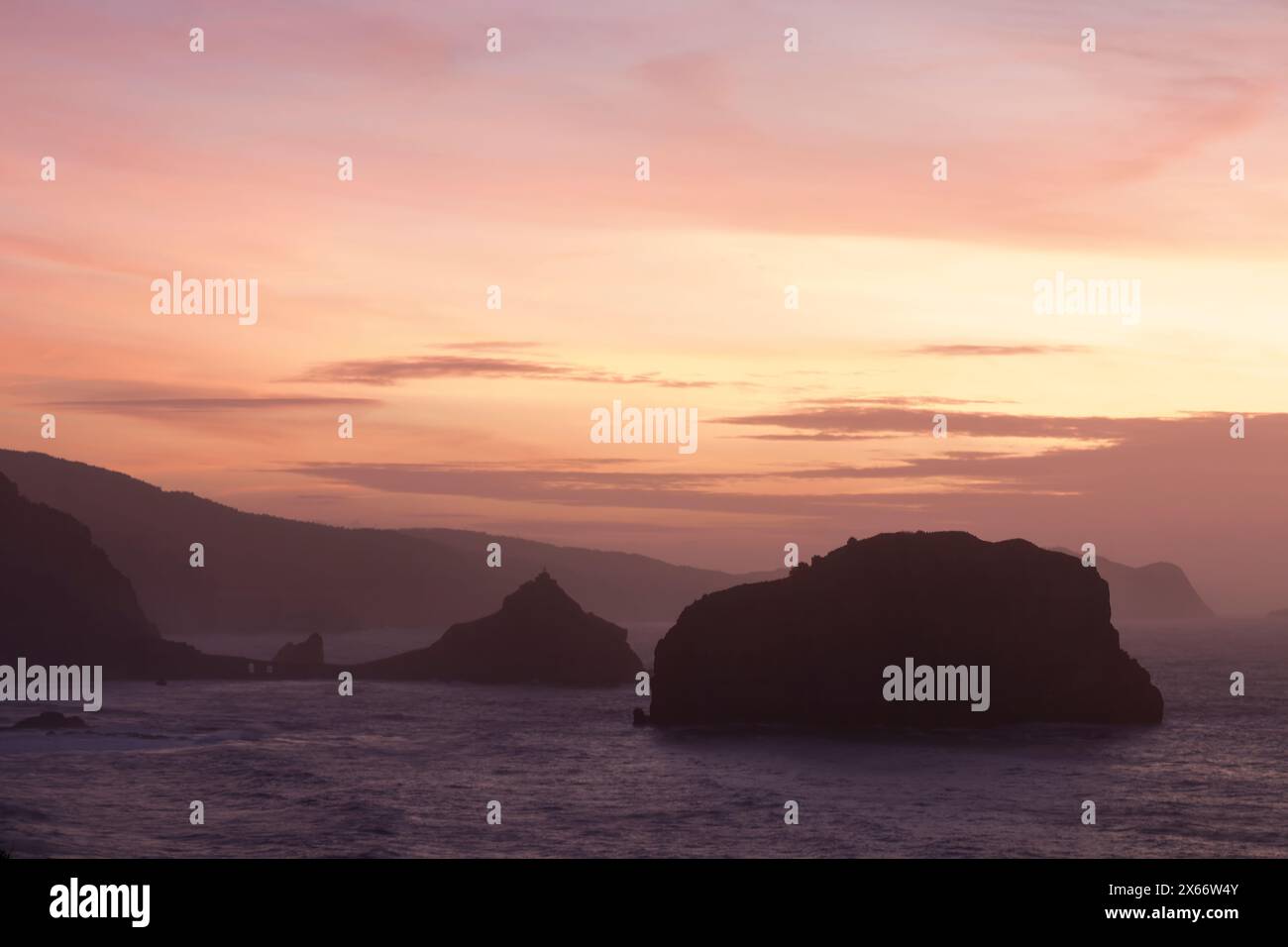 serene sunset over the ocean, with silhouetted rocky islands and warm hues of pink and orange in the sky Stock Photo