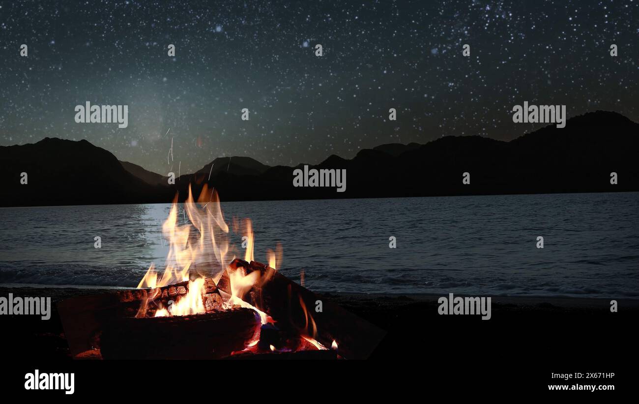a bonfire burns at night against the background of mountains and sea with bright stars.. Stock Photo