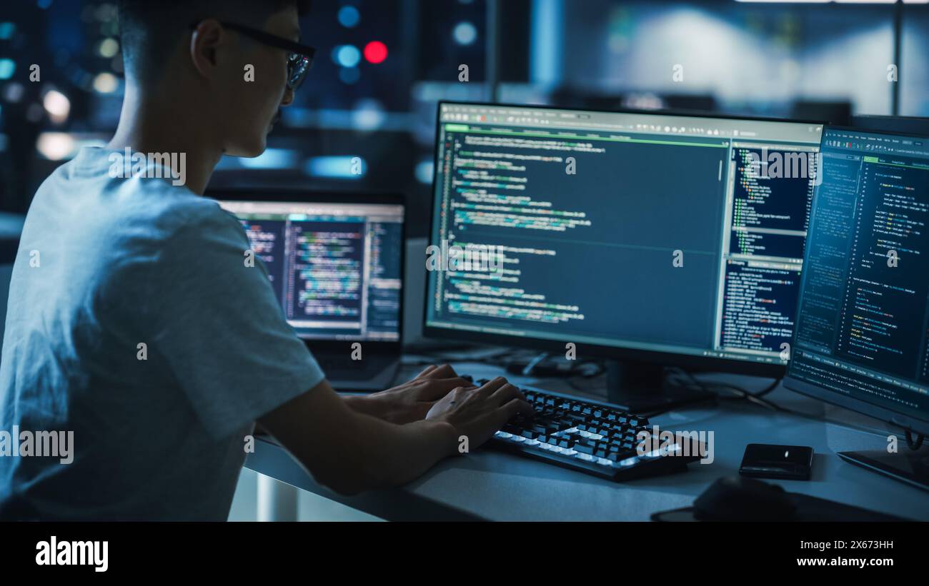 Night Office: Young Handsome Man in Working on Desktop Computer. Digital Entrepreneur Typing Code, Developing Modern Software, e-Commerce App Design, Developing of e-Business. Over Shoulder Stock Photo