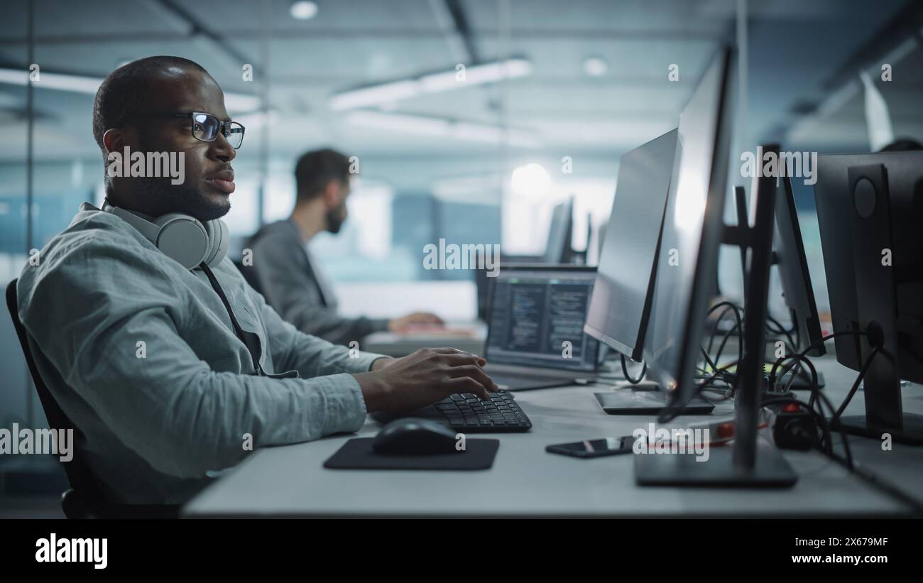 Authentic Office: Enthusiastic Black IT Programmer Starts Working on Desktop Computer. Male Website Developer, Software Engineer Developing App, Video Game. Terminal with Coding Programming Language Stock Photo