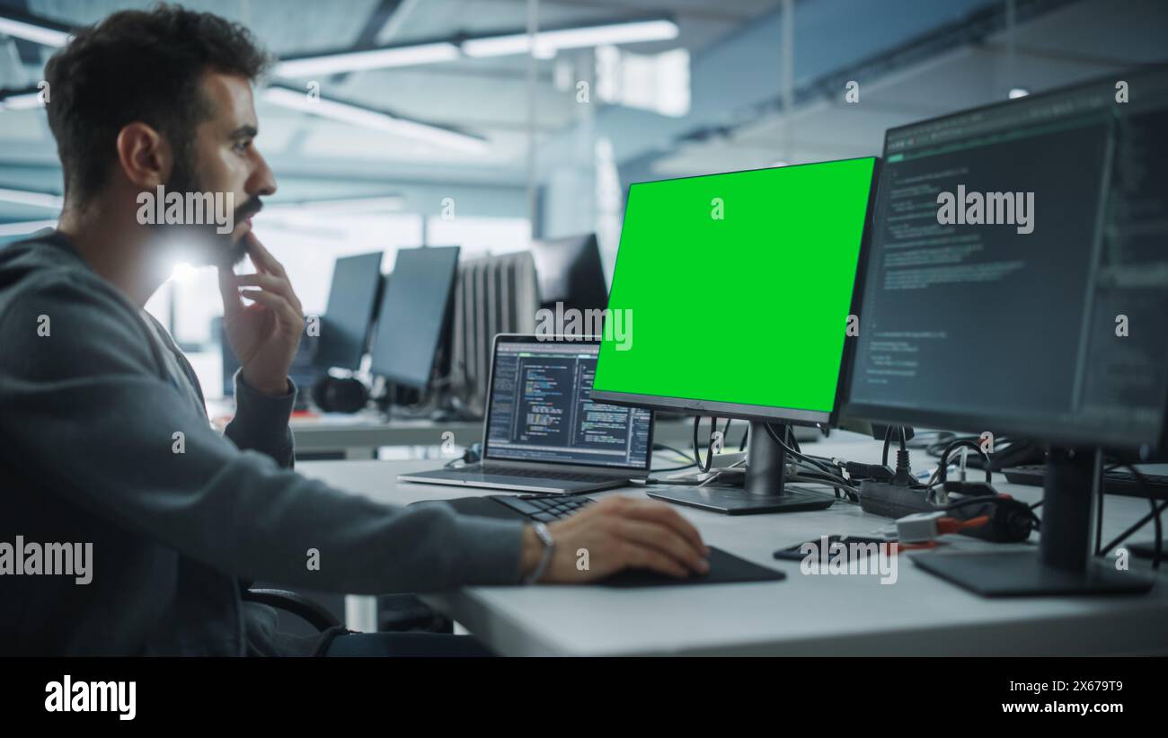 Multi-Ethnic Office: White IT Programmer Working on Computer with Green Screen Chroma Key Display. Male Software Engineer Developing App, Program, Video Game. Terminal with Code Language. Stock Photo
