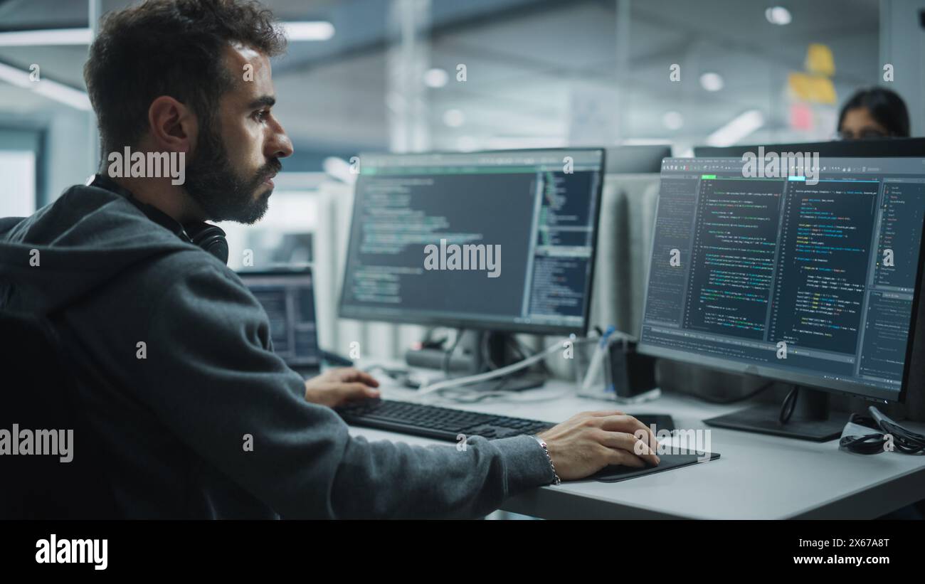 Diverse Office: IT Programmer Working on Desktop Computer. Male Specialist Creating Innovative Software Engineer Developing App, Program, Video Game. Terminal with Coding Language. Over Shoulder Stock Photo