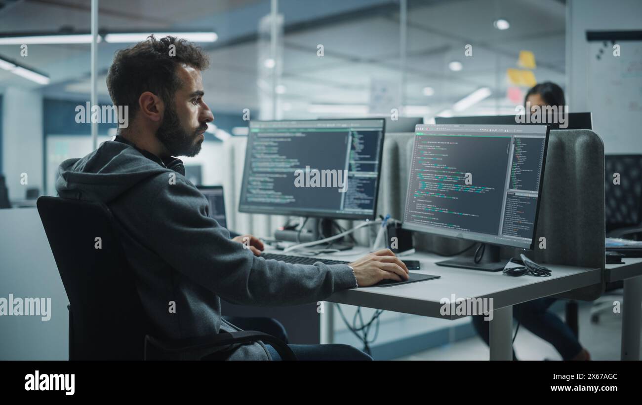 Diverse Office: IT Programmer Working on Desktop Computer. Male Specialist Creating Innovative Software Engineer Developing App, Program, Video Game. Terminal with Coding Language. Over Shoulder Stock Photo