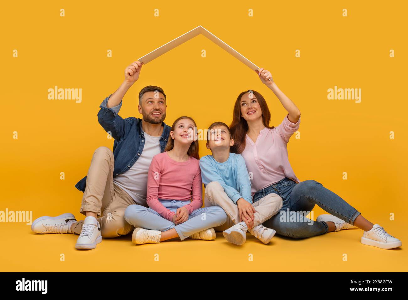Family of Four Imagining Home Together Against Bright Yellow Background Stock Photo