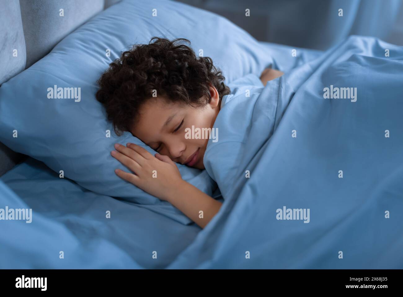 Young Boy Sleeping in Bed With Blue Sheets at Night Stock Photo