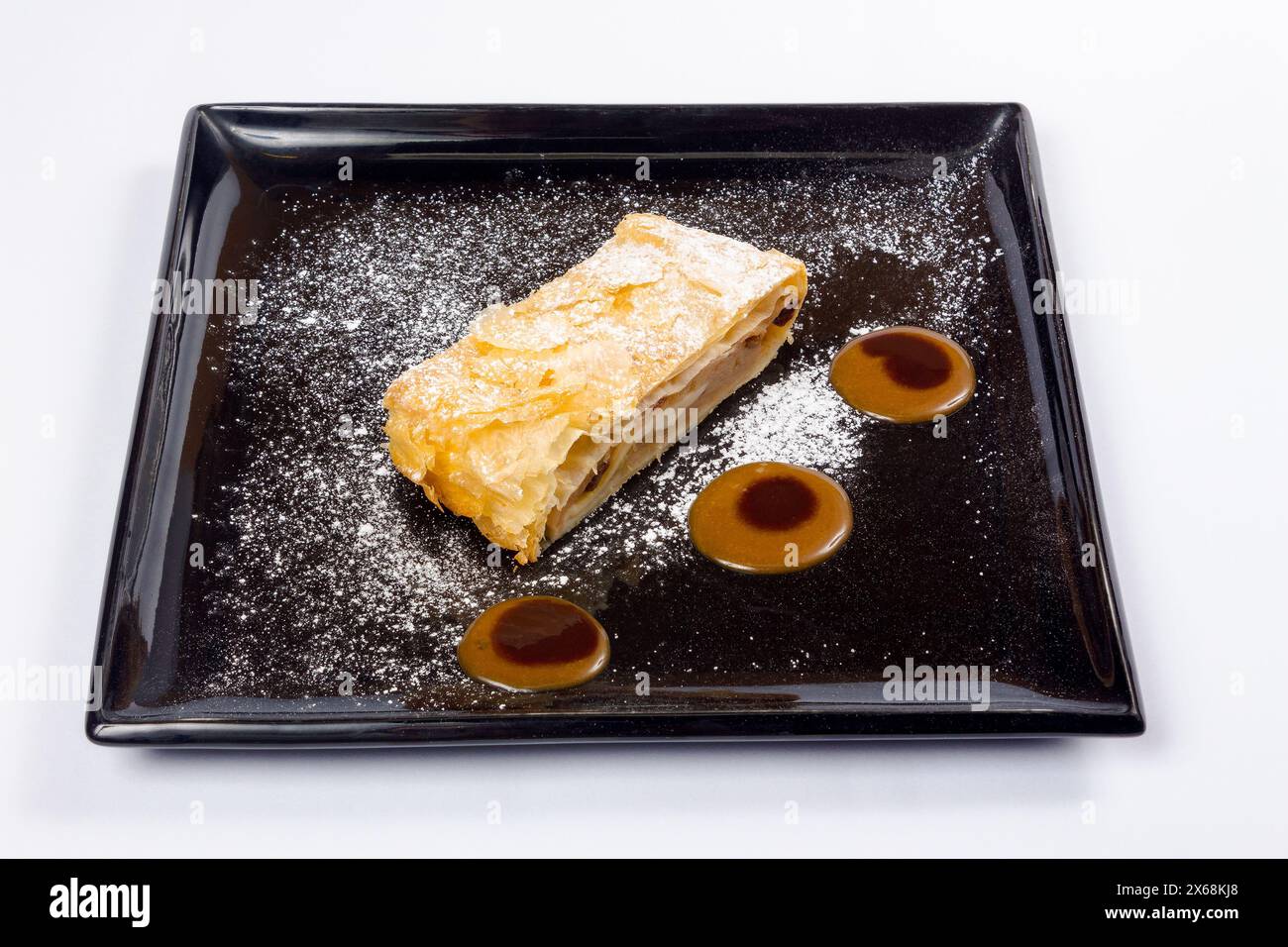 delicious strudel decorated with powdered sugar and cream on a black plate. Stock Photo