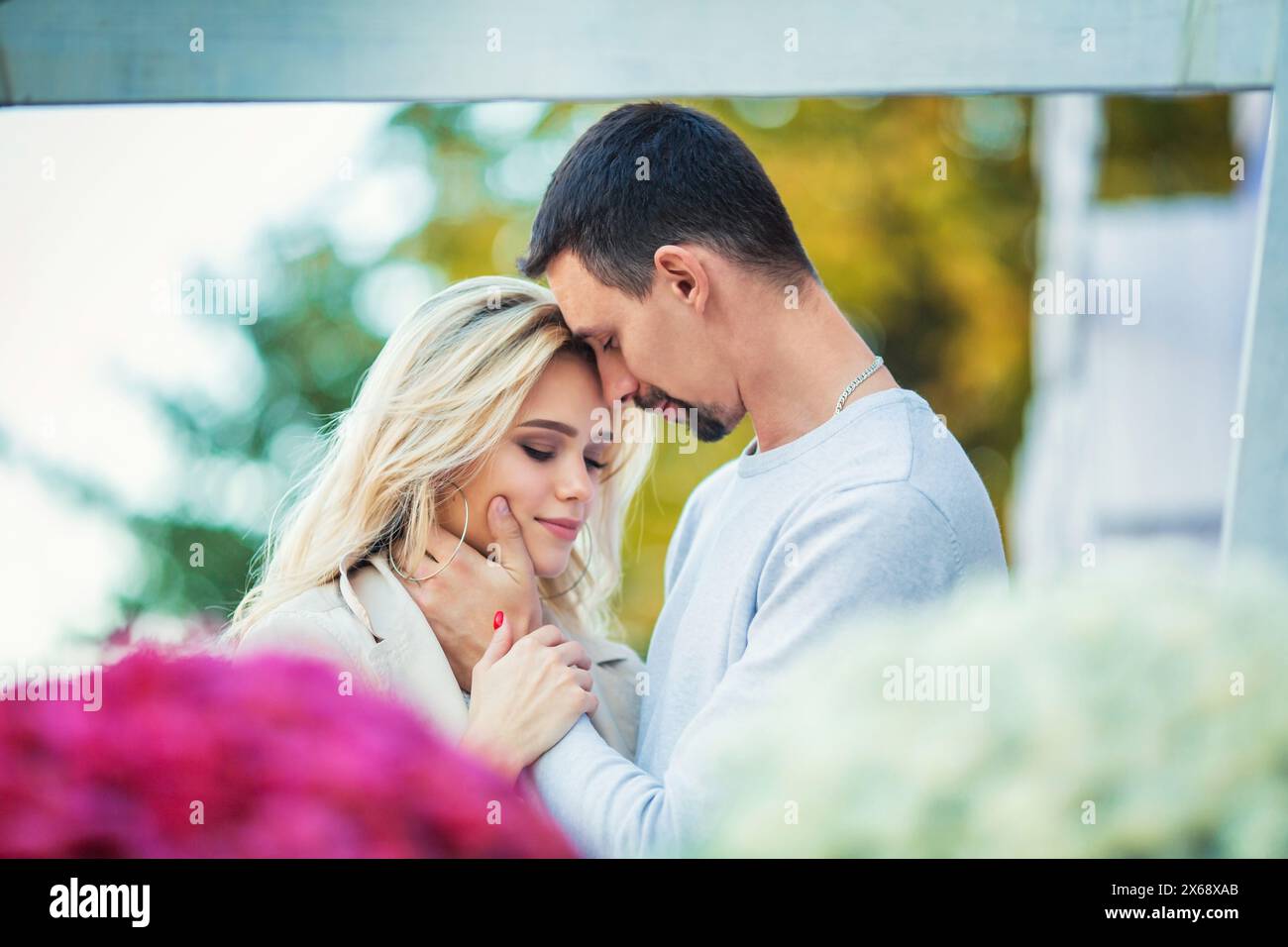 Love story engagement session of a happy young caucasian straight couple in white sweaters, boyfriend is hugging girlfriend, emotionally holding her f Stock Photo