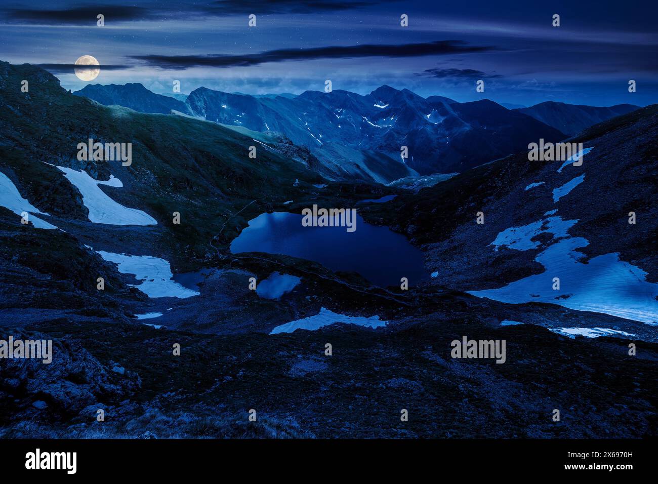 glacier lake among rocky hills at night. mountainous landscape in full moon light Stock Photo