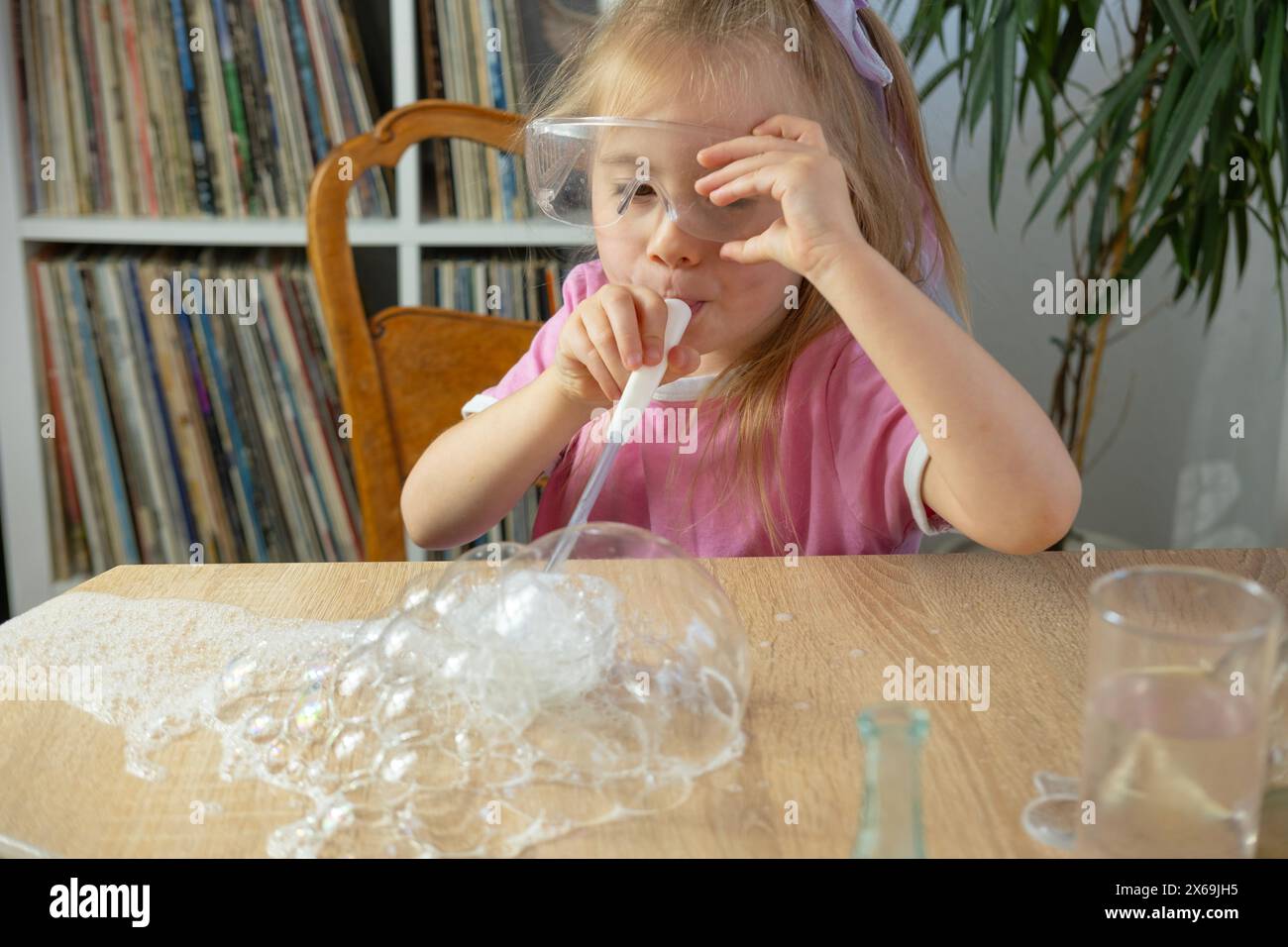 Little girl blows bubbles through plastic straw made of soap foam, kids fun games, diy soap bubbles, making experiment Stock Photo