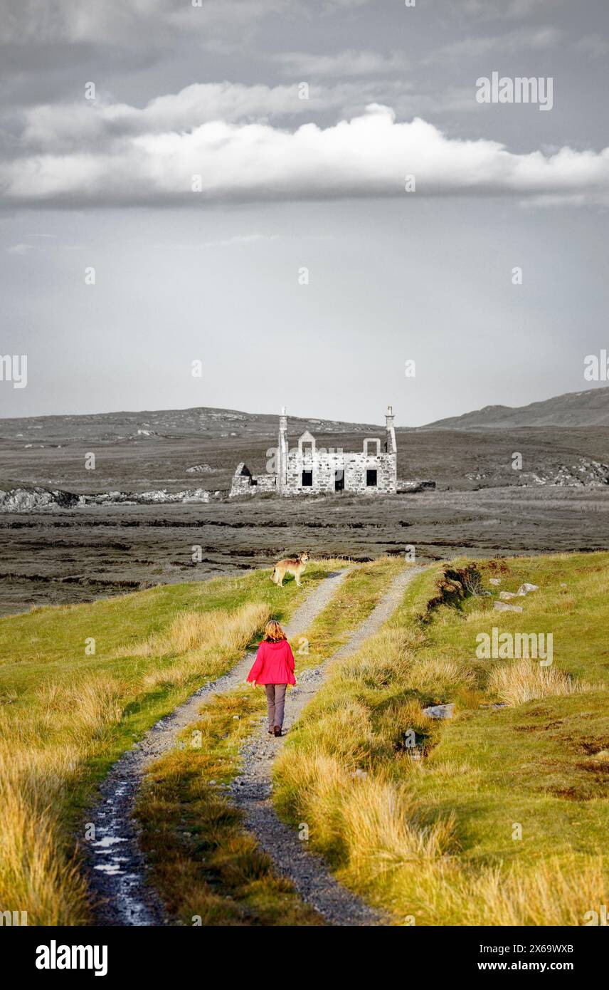 Abandoned ruined crofters house croft at Minish. West end of Loch Maddy. North Uist, Outer Hebrides, Scotland. Woman and dog walking on path Stock Photo