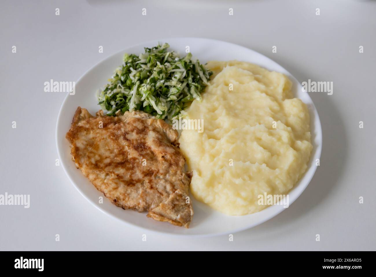 A delicious breakfast or lunch with mashed potatoes, chop with salad - green onions and green young cabbage, parsley on the white plate. Stock Photo