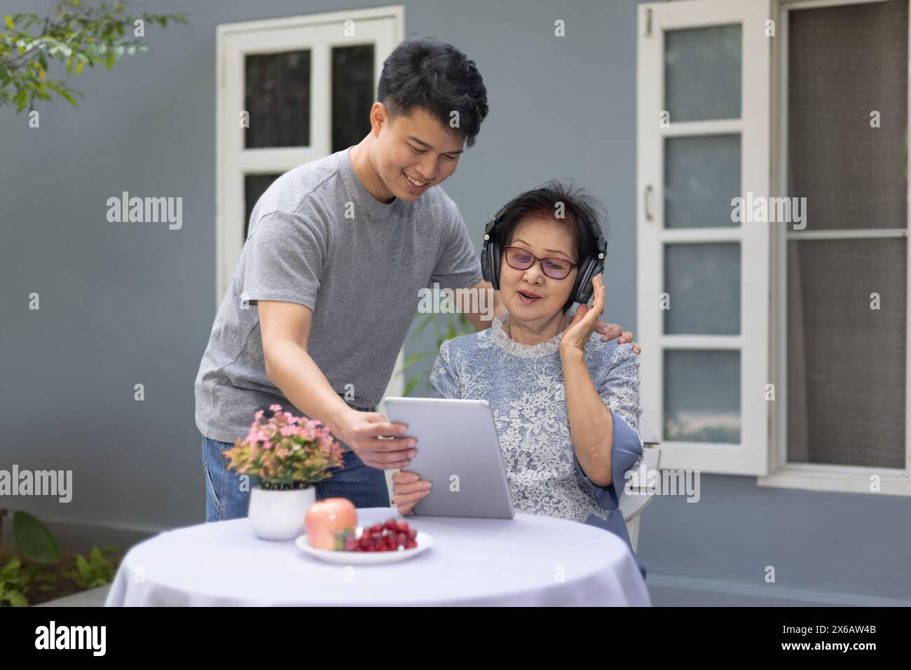 Grandson helping grandmother using computer tablet for listen music and pose share good news at social media. Stock Photo