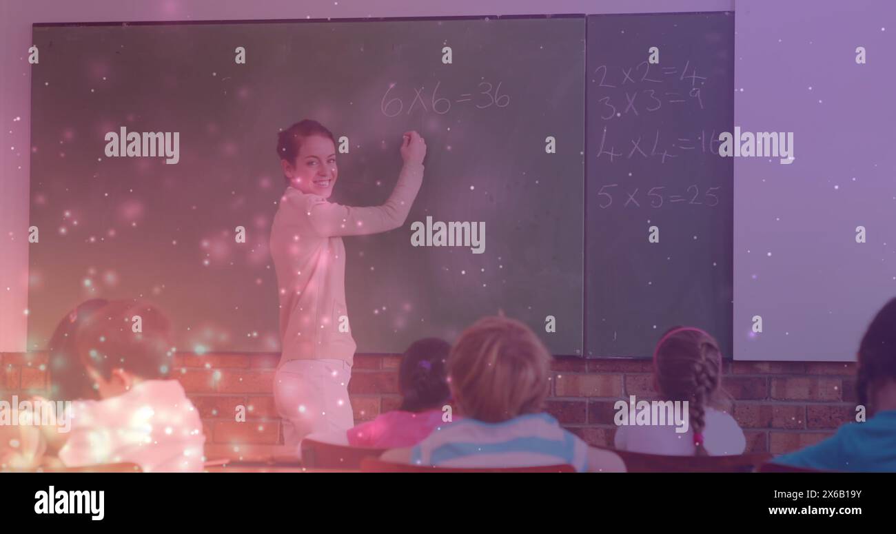Image of light spots over caucasian female teacher writing on board with diverse schoolchildren Stock Photo