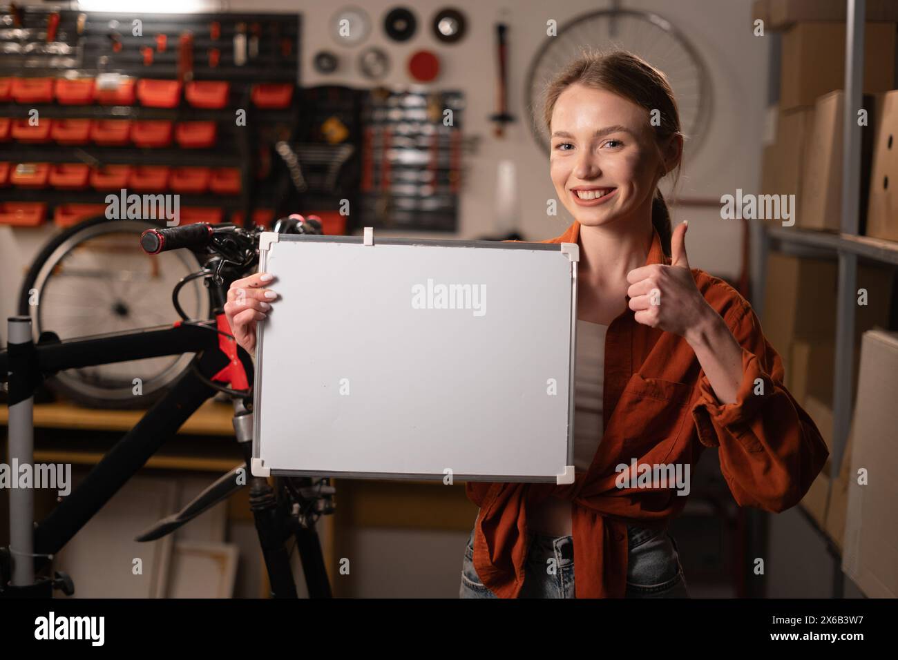 Beautiful Young female mechanic Holding white board With Copy Space For Advertisement, repairman demonstrating white empty billboard with place for Stock Photo