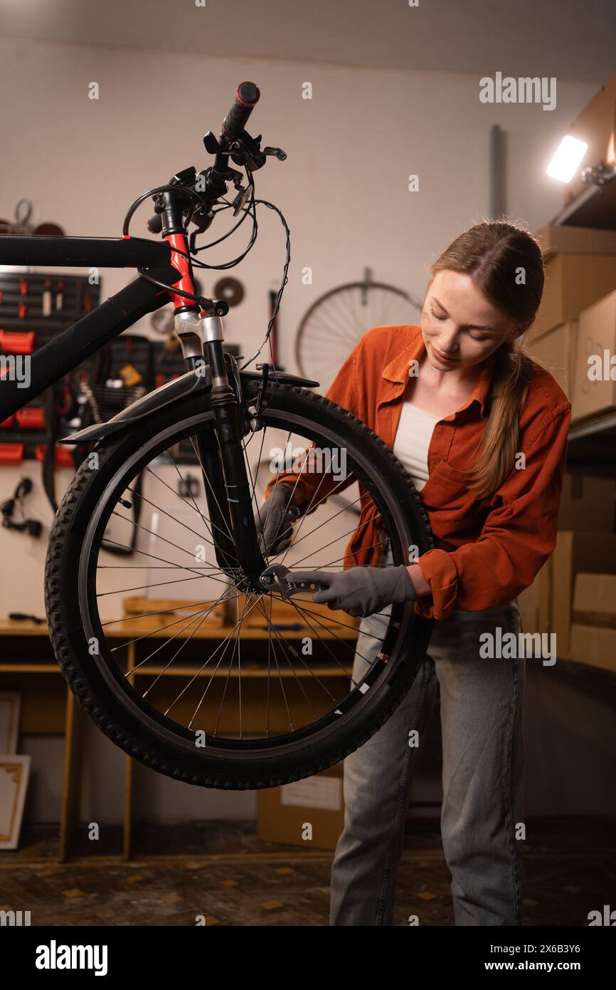 Blonde woman repairing her bike. Lady fixing her bicycle while working on home garage. Bicycle Mechanic. Stock Photo