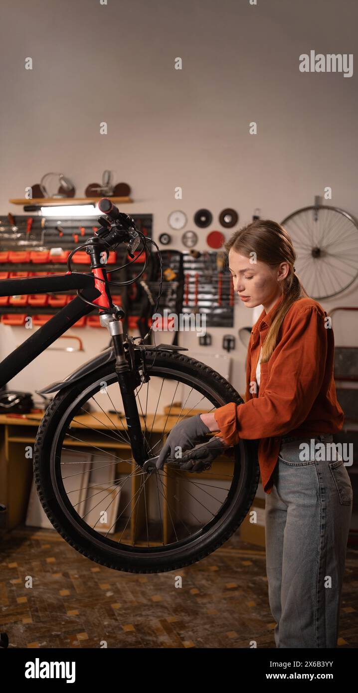 Beautiful female worker repairing bicycle. Bike workshop or garage interior. Stock Photo