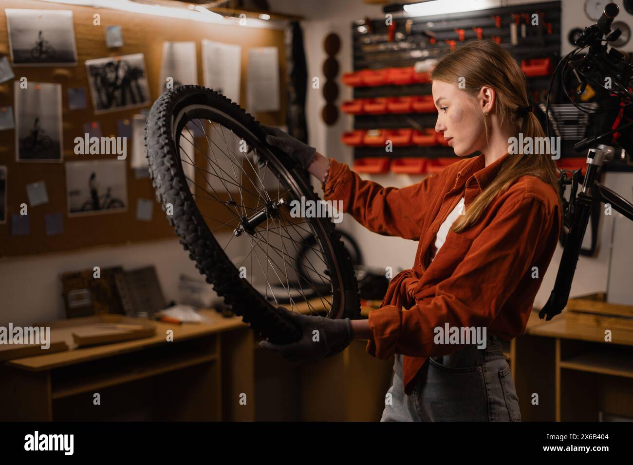 Young woman bicycle mechanic fixing cycle wheel in repair shop. Bike shop engineer fix bicycle wheel in workshop. bike part in female hands. Stock Photo