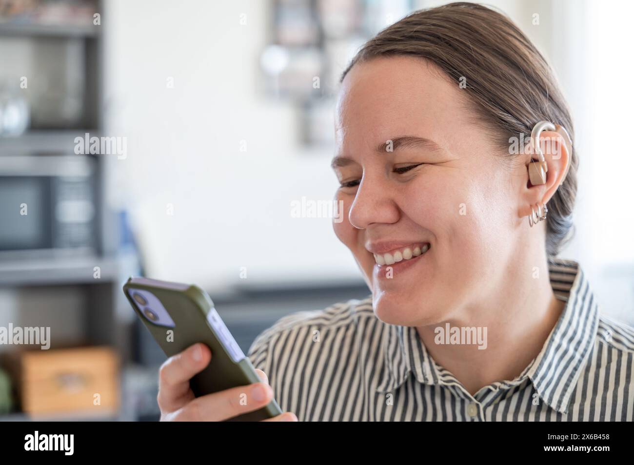 Woman with hearing aid using smartphone and smiling Stock Photo