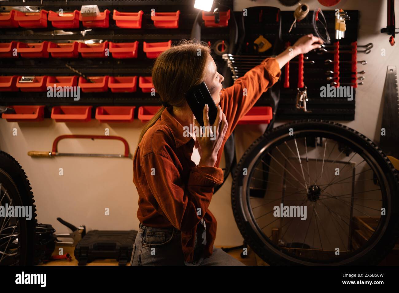 Bicycle maintenance and repair concept. Young blonde woman working in garage calling on mobile phone consulting with mechanic Stock Photo