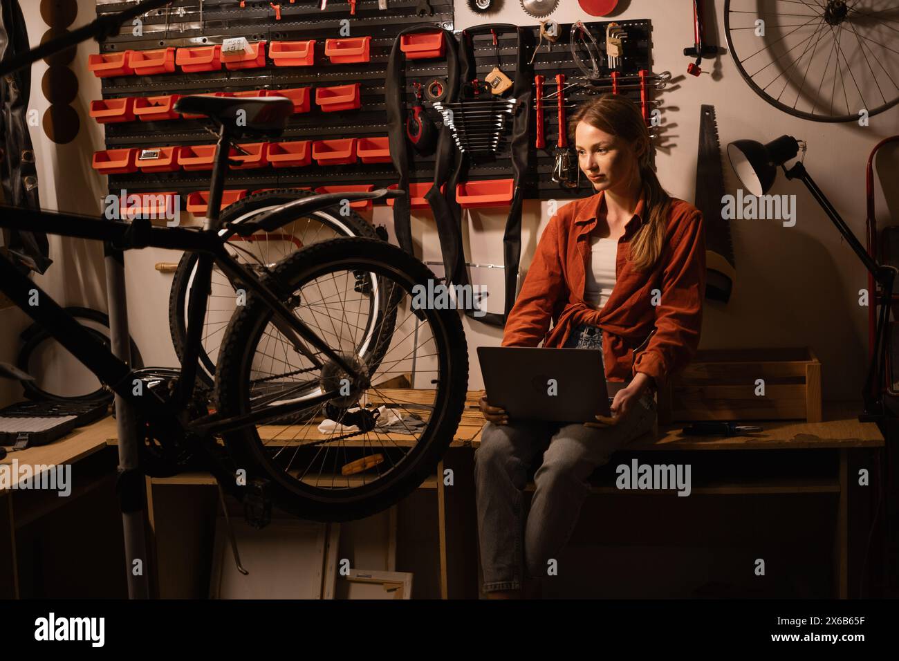 Female mechanic in her Workshop or garage looking at laptop. Bike shop owner with laptop. Stock Photo