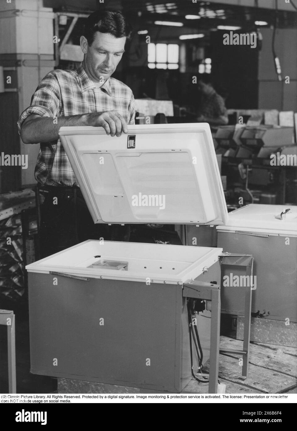 Freezer in the 1950s. Final testing and installation of new freezers in a factory. A man is seen assembling and mounting the lid of a freezer. Deep-frozen food would be the start of a revolution in household habits and food storage. Many were sceptical, and especially canned food manufacturers considered frozen food to be a passing trend. Sweden 1955 Stock Photo