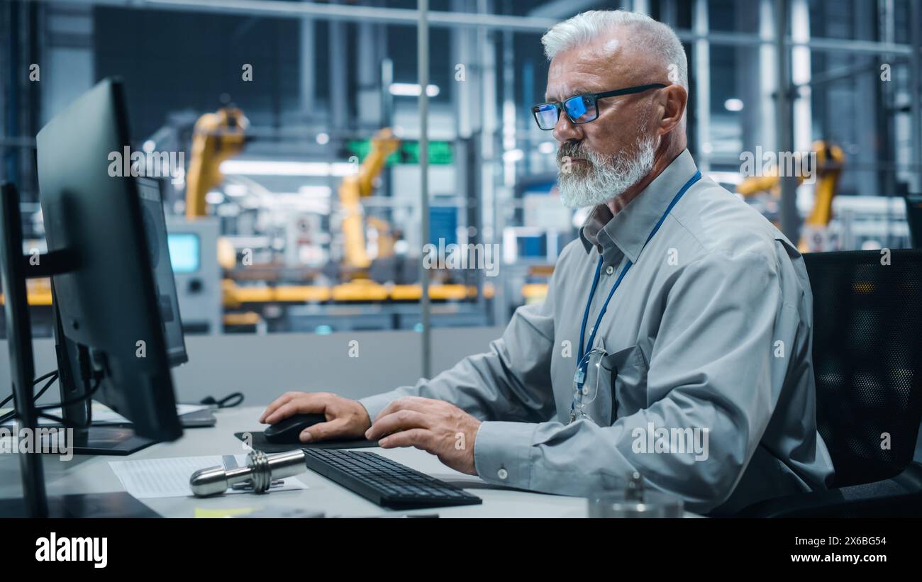 Car Factory Office: Portrait of Male Engineer Working on Computer. Automated Robot Arm Assembly Line Manufacturing Electric Vehicles. Technician Monitoring Electronics Production Conveyor. Stock Photo