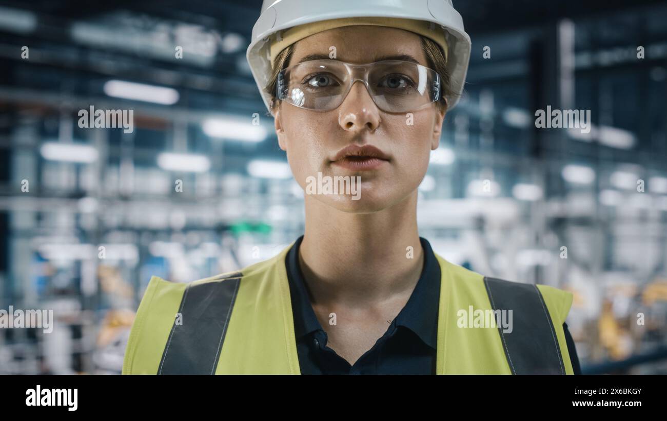 Portrait of Female Automotive Industry Engineer Putting on Safety Glasses at Car Factory Facility. Confident Assembly Plant Specialist Working on Manufacturing Modern Electric Vehicles. Stock Photo