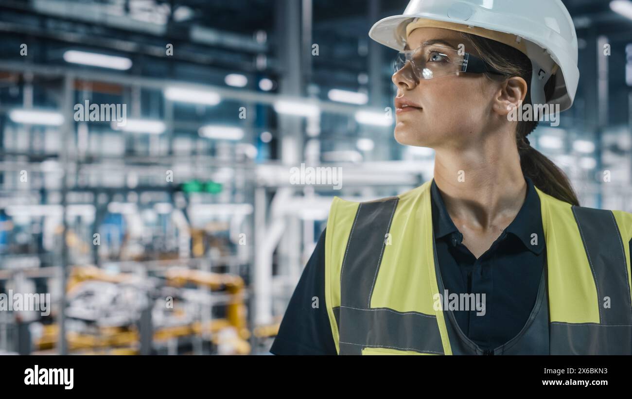 Portrait of Female Automotive Industry Engineer Wearing Safety Glasses and High Visibility Vest at Car Factory Facility. Confident Assembly Plant Specialist Working on Manufacturing Modern Vehicles. Stock Photo