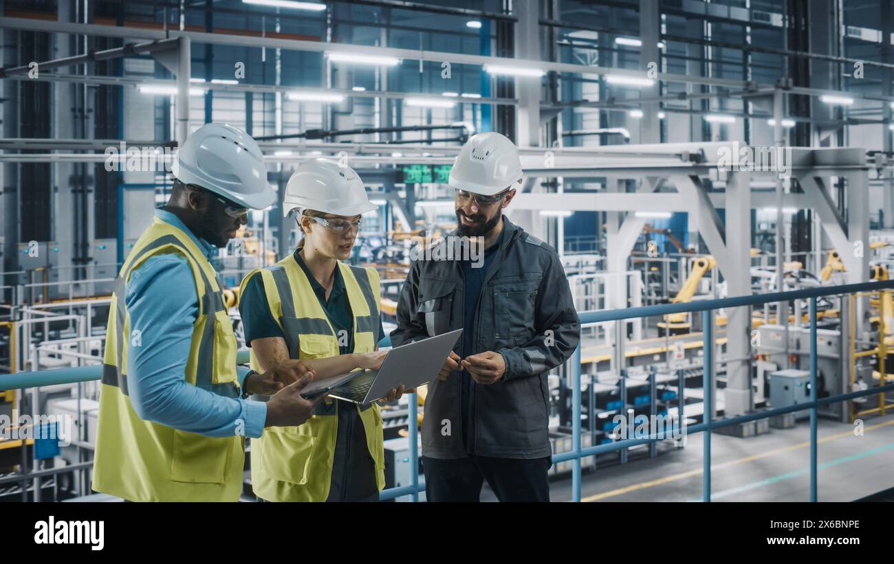 Young Diverse Team of Car Factory Specialists Working on Laptop and Tablet Computers. Engineers Discussing Automotive Industrial Manufacturing Technology on Modern Vehicle Assembly Plant. Stock Photo