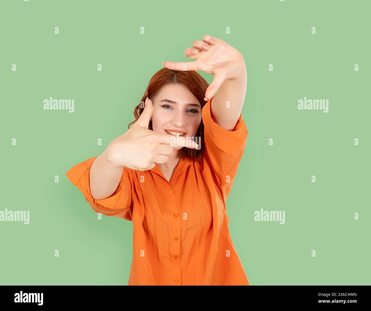 portrait of selective focus young caucasian woman making frame with hands. Looking through. Photography concept idea, isolated green studio background Stock Photo