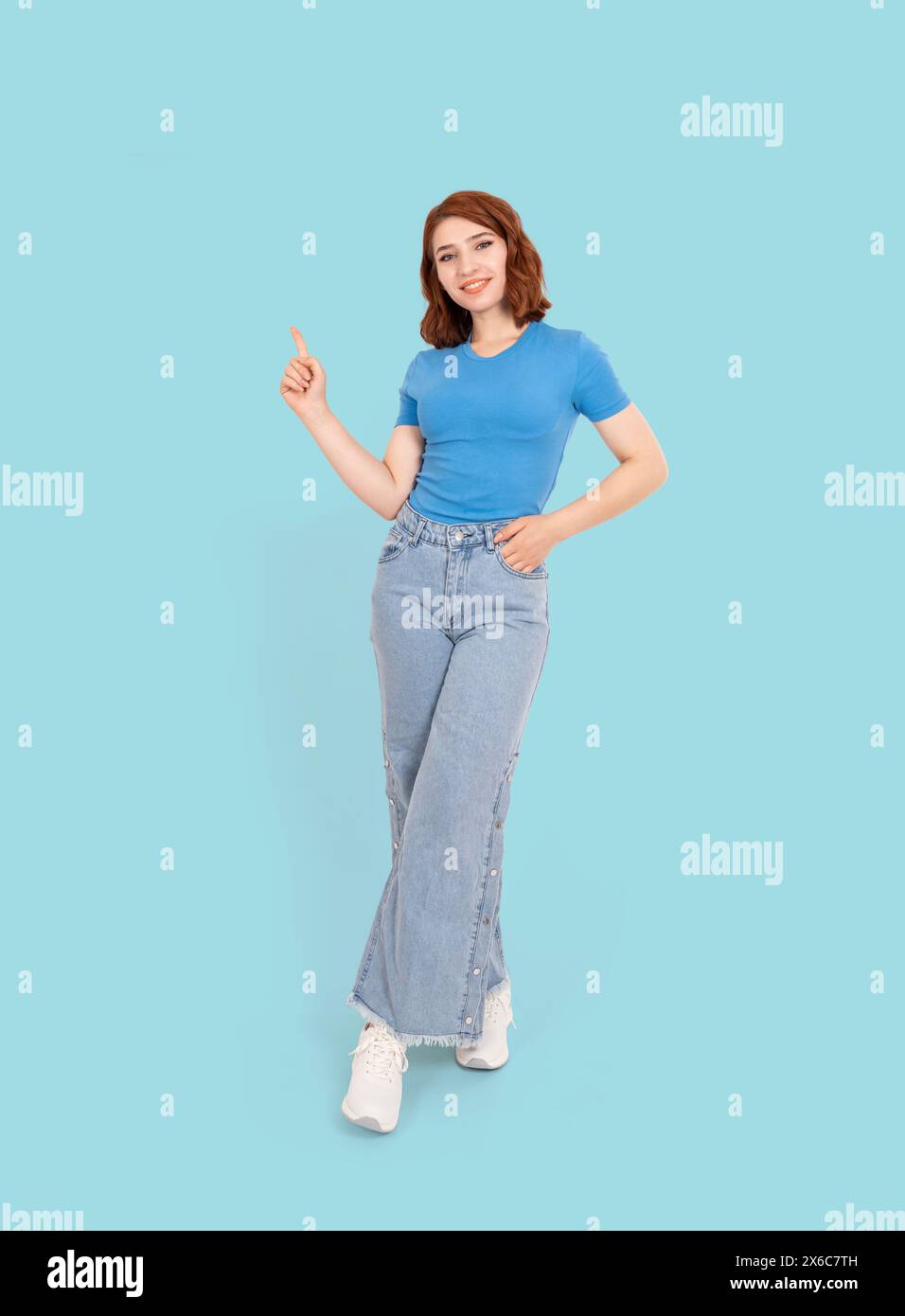 Full body view red hair young caucasian girl showing copy space. Wearing casual blue t-shirt and jeans. Pointing index finger workspace Stock Photo