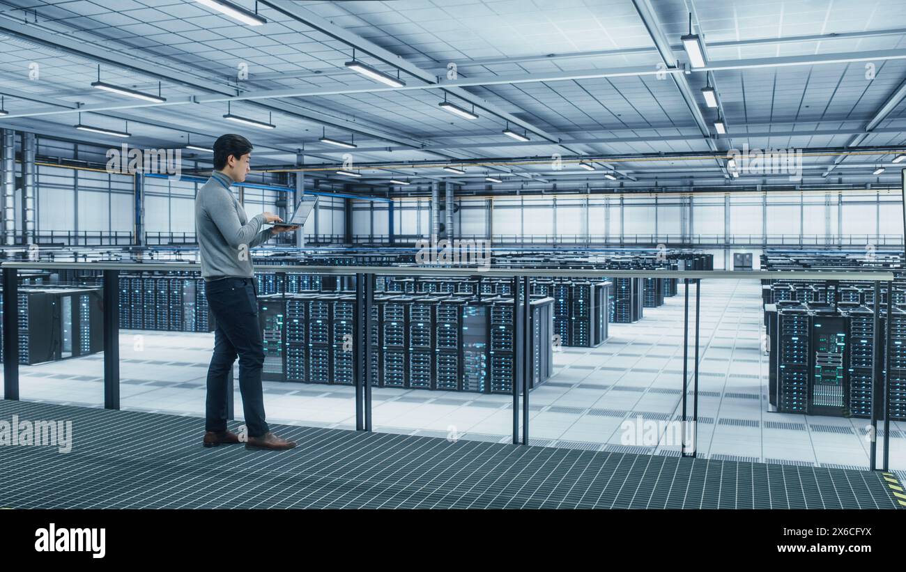 Data Center Engineer Using Laptop Computer. Server Farm Cloud Computing Specialist Facility with Asian Male System Administrator Working with Data Protection Network for Cyber Security. Stock Photo