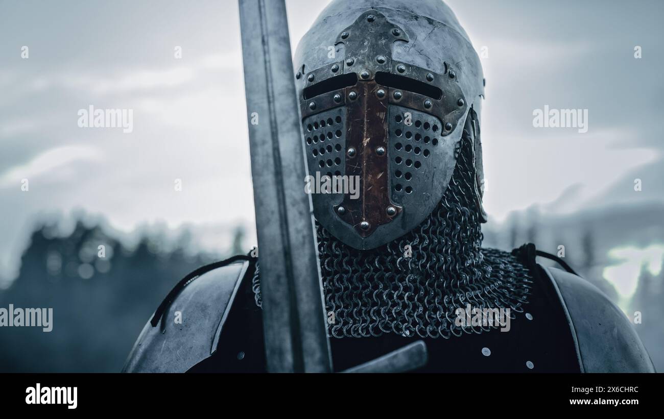 Medieval Knight Wearing Armour and Helmet, Draws Sword from Shearh, Ready to Fight, Kill His Enemy in Battle. Warrior Soldier on Battlefield. War, Invasion, Crusade. Cinematic Historic Reenactment Stock Photo