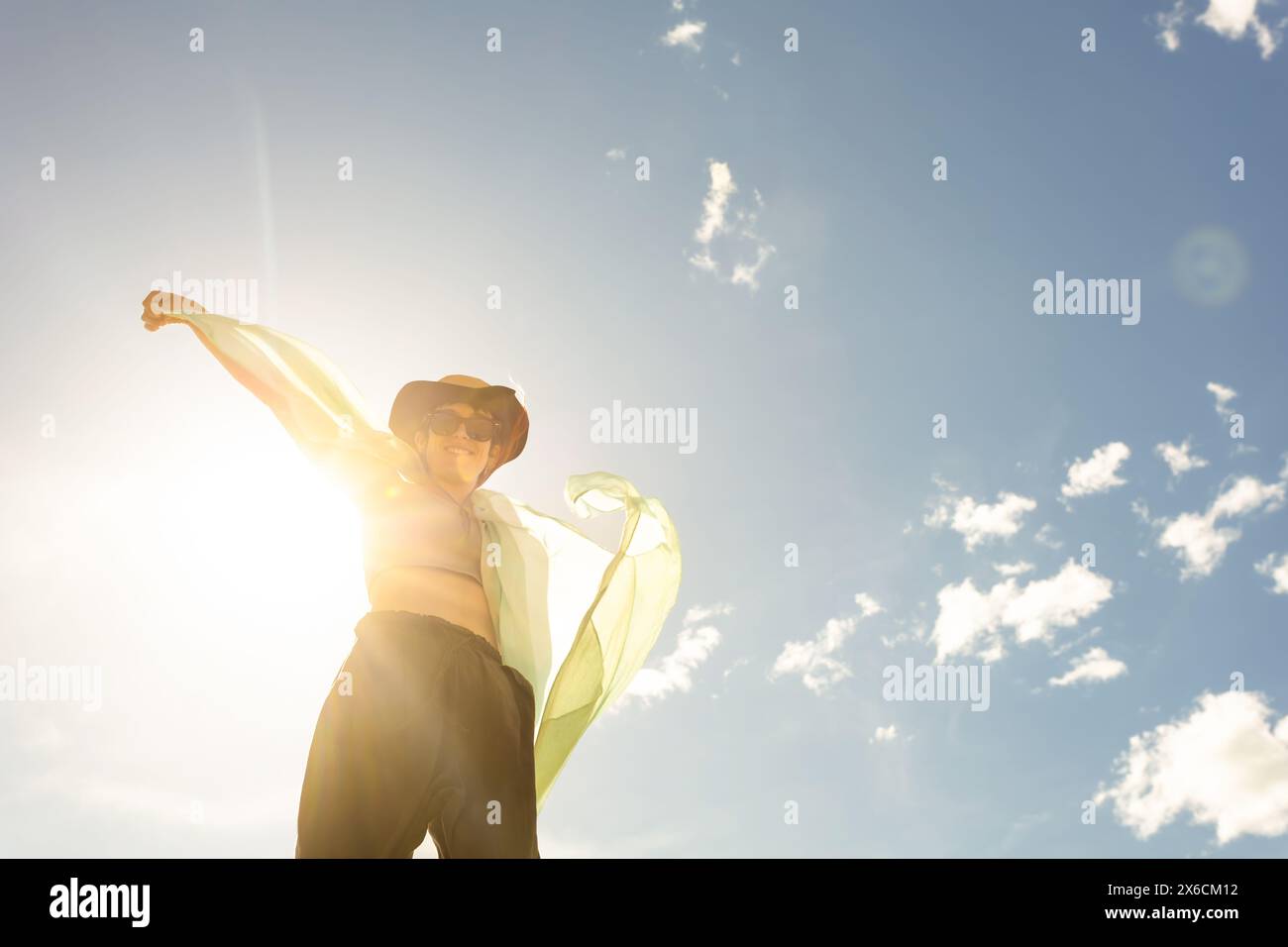 woman with scarf, handkerchief, cap and sunglasses at sunset, lens flare, wind clouds background smiling face blue sky, dancing Stock Photo