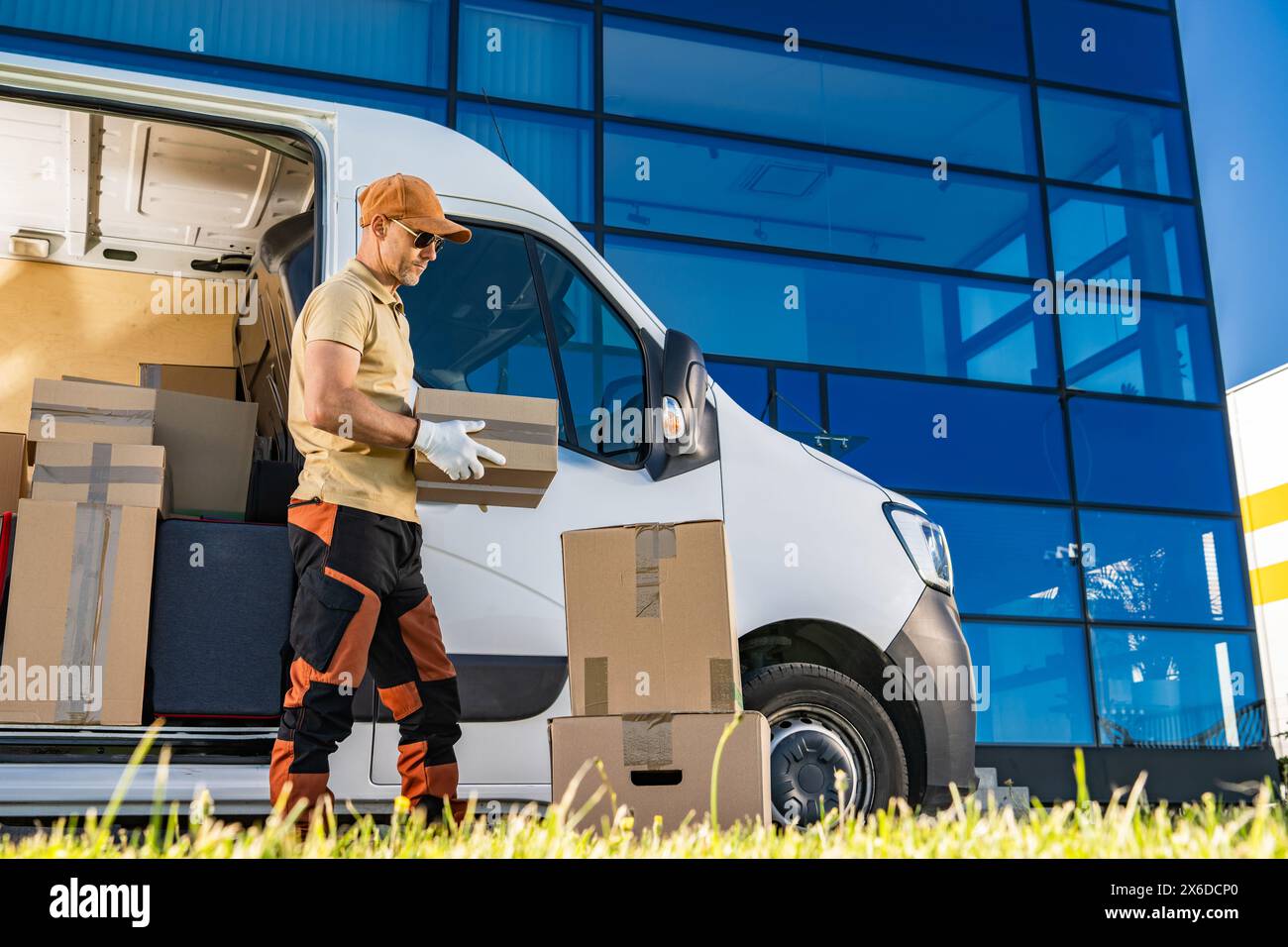 Caucasian courier loading boxes into van in front of building. Stock Photo