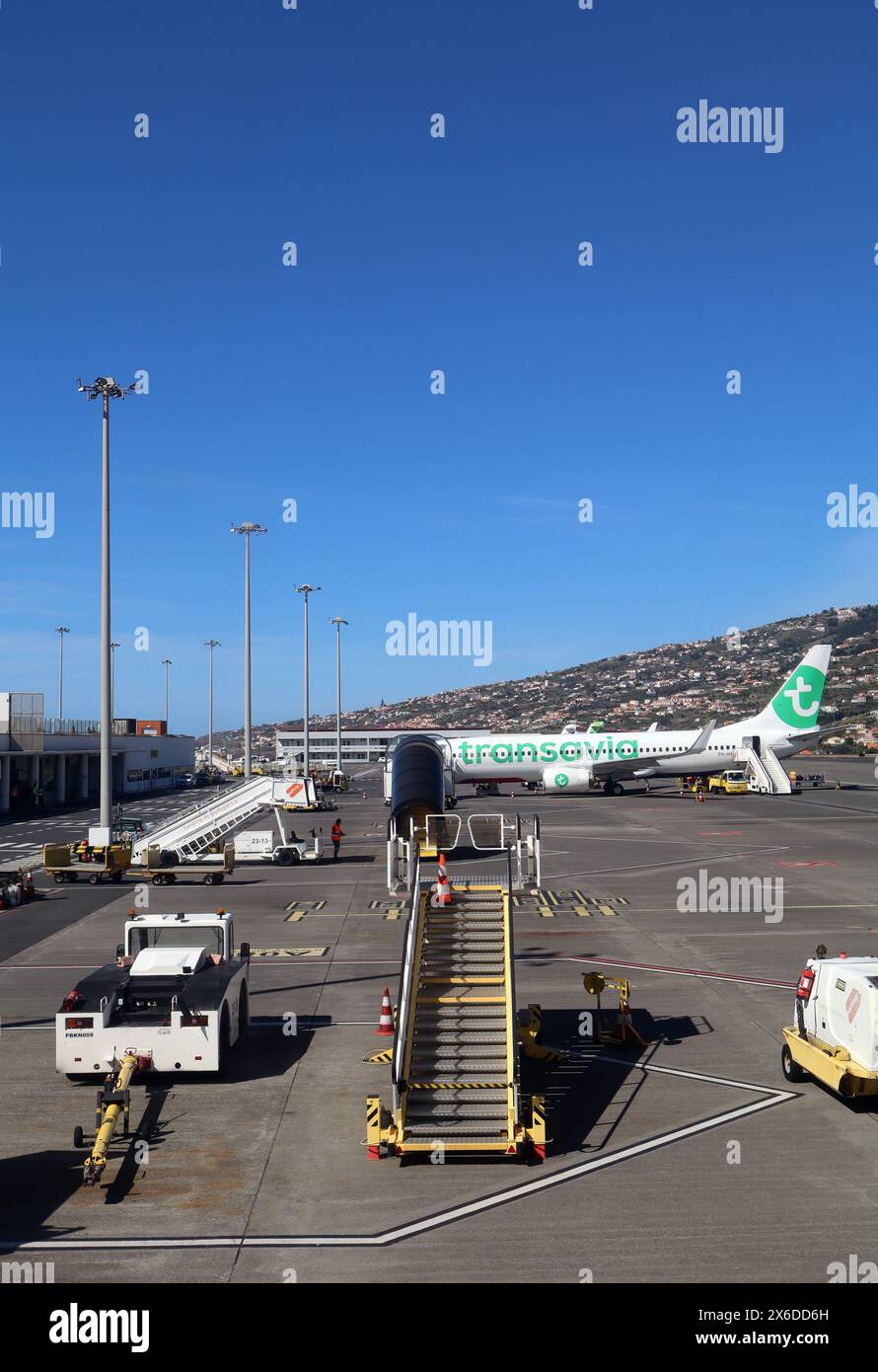 Transavai Boeing 737-8K2 on apron by terminal building Cristiano Ronaldo International airport, Madeira on 3rd May 2024 and assorted airport equipment. Stock Photo