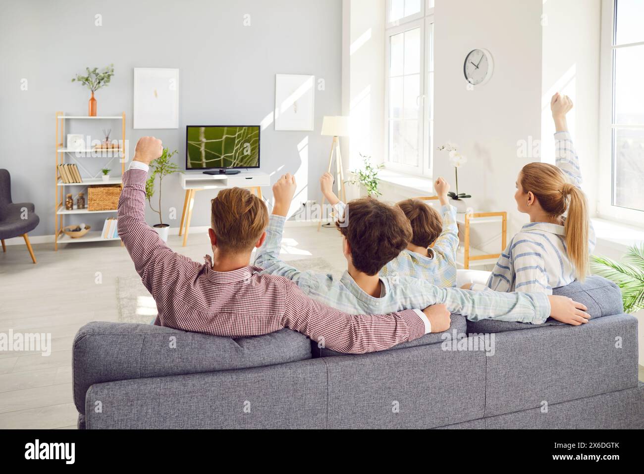 Back view of family fans sitting on sofa and watching football match on tv rejoicing scoring goal. Stock Photo