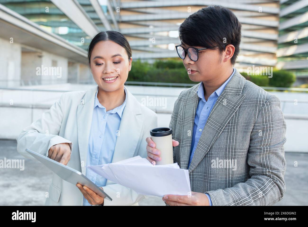 Two Asian Business People Examining Document, Checking Tablet Stock Photo