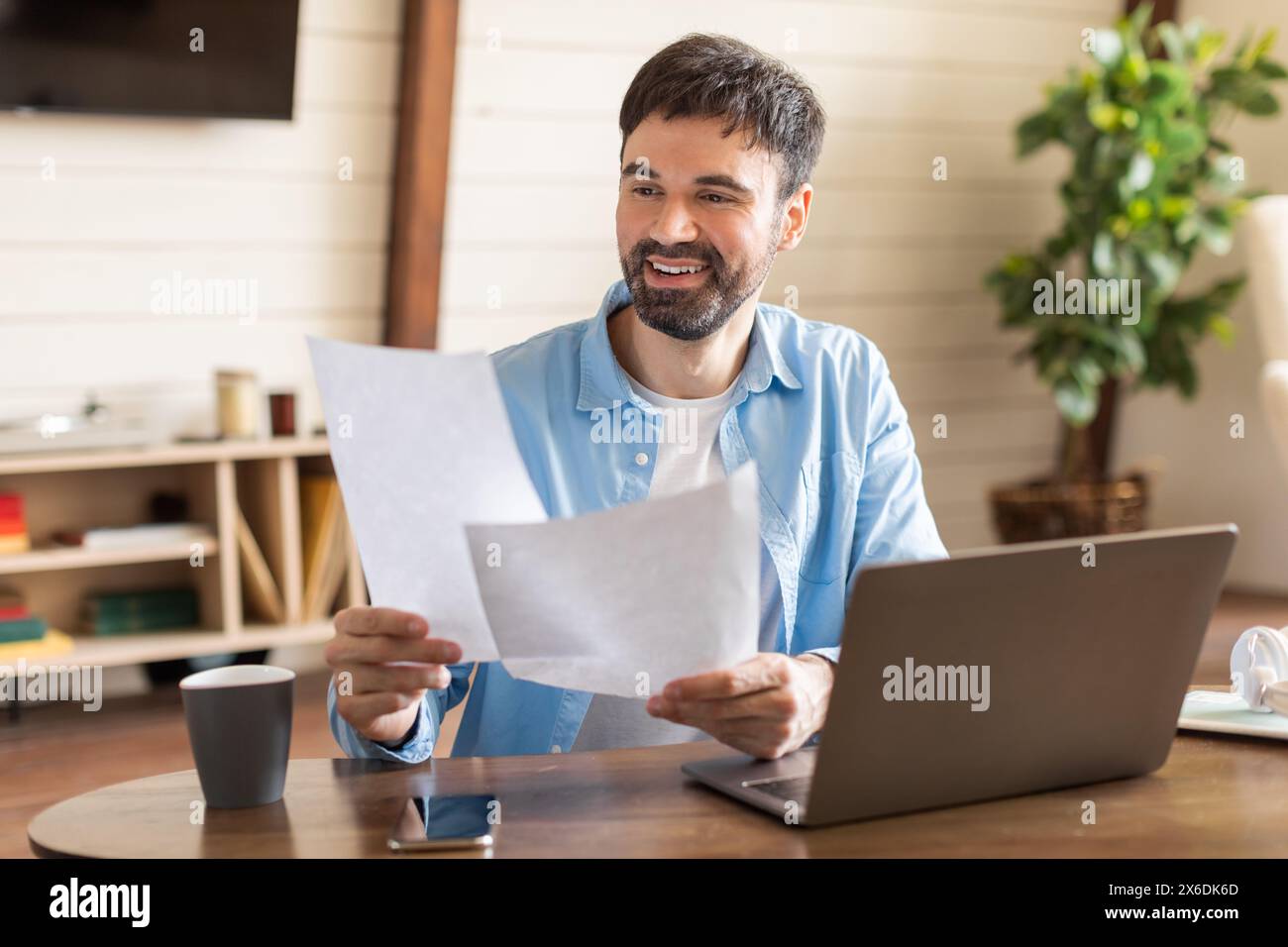 Man Sitting at Table Holding Piece of Paper Stock Photo