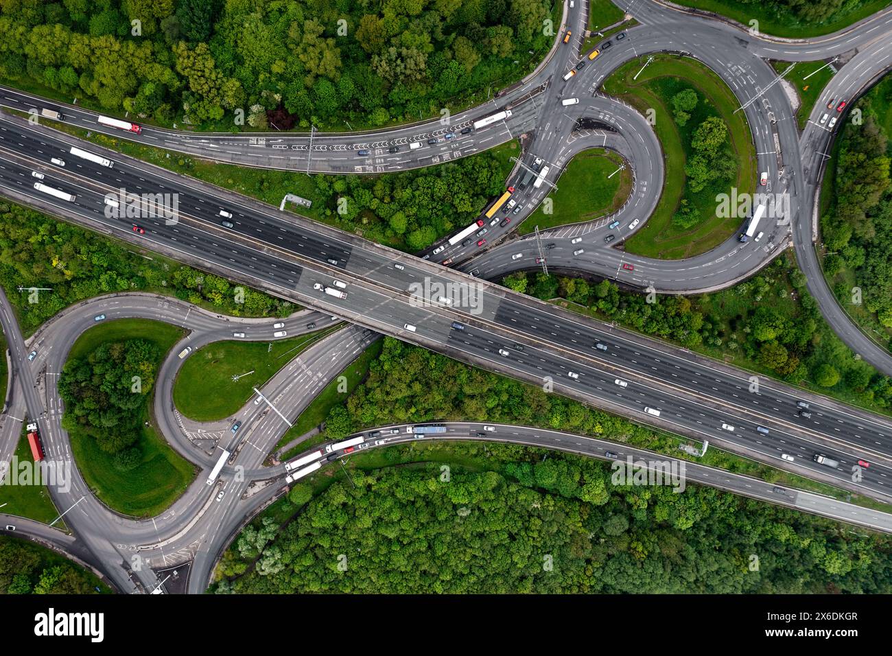 Aerial view directly above a major UK motorway junction with roundabout and bridge cutting through green woodland in an environmental issue concept Stock Photo