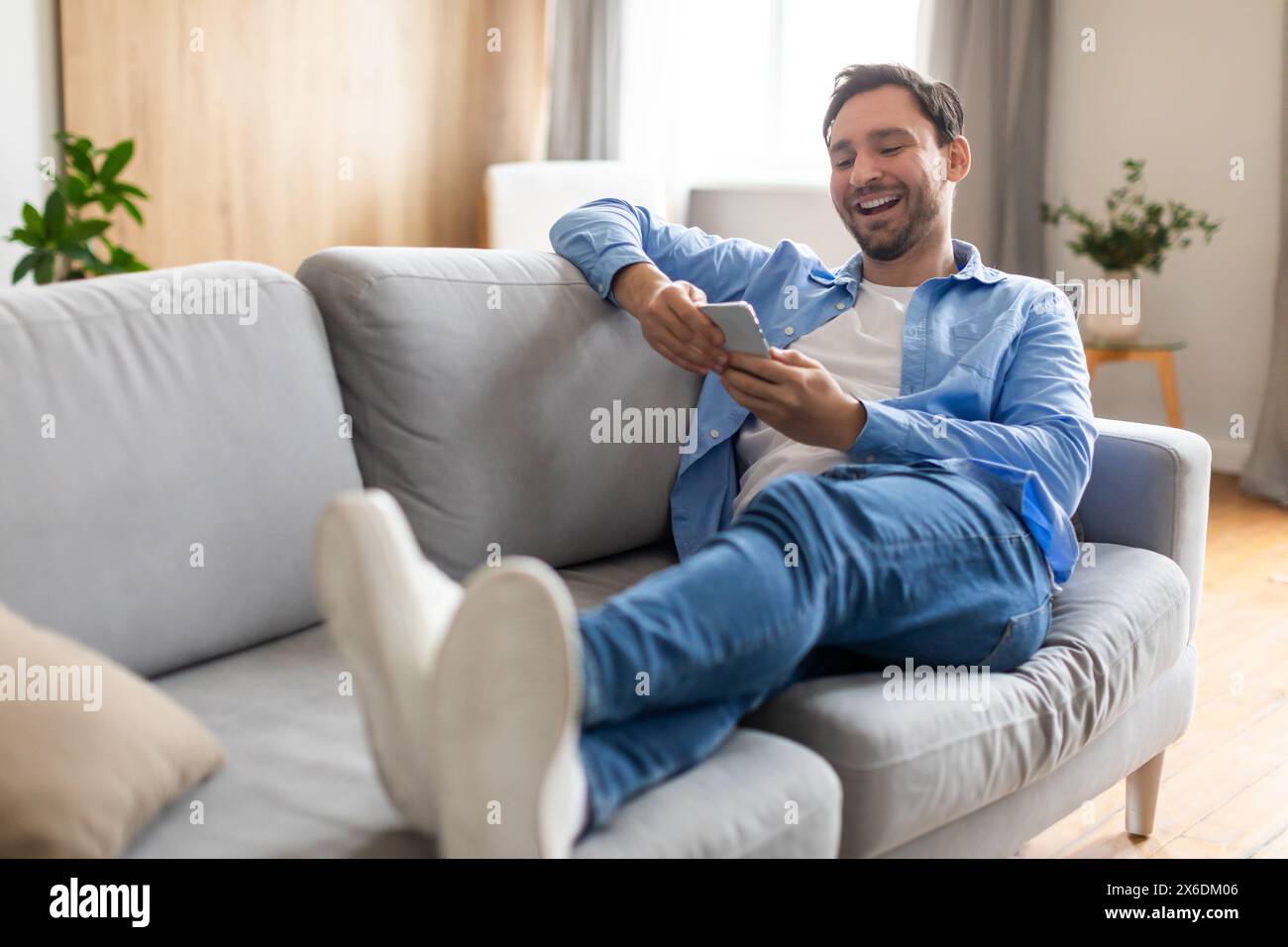 Happy Man Reclining on Couch Using Phone Stock Photo