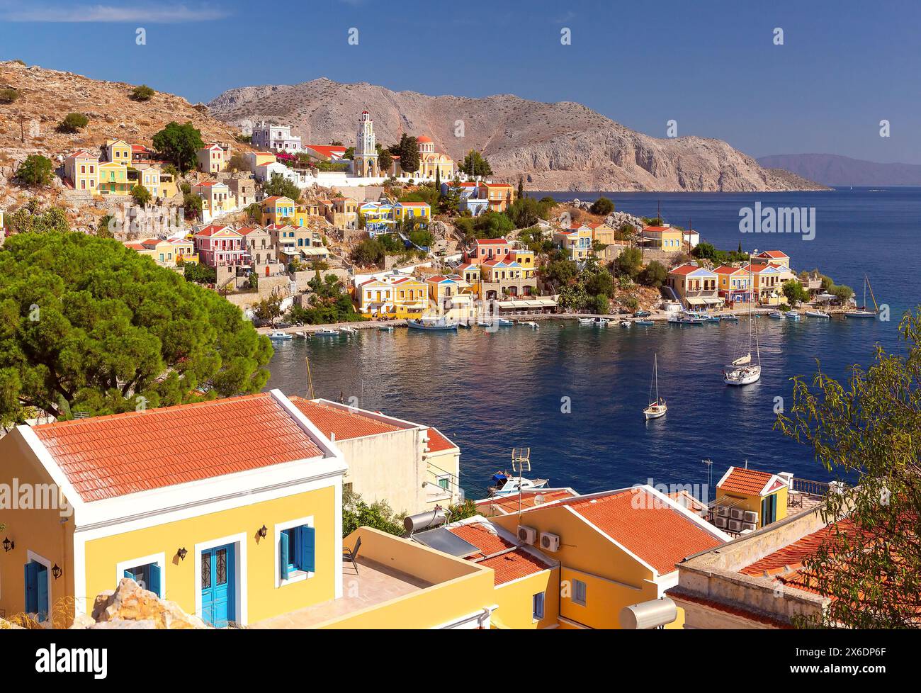 Wide panoramic shot of Symi Island with colorful houses against scenic mountain backdrop, Greece Stock Photo