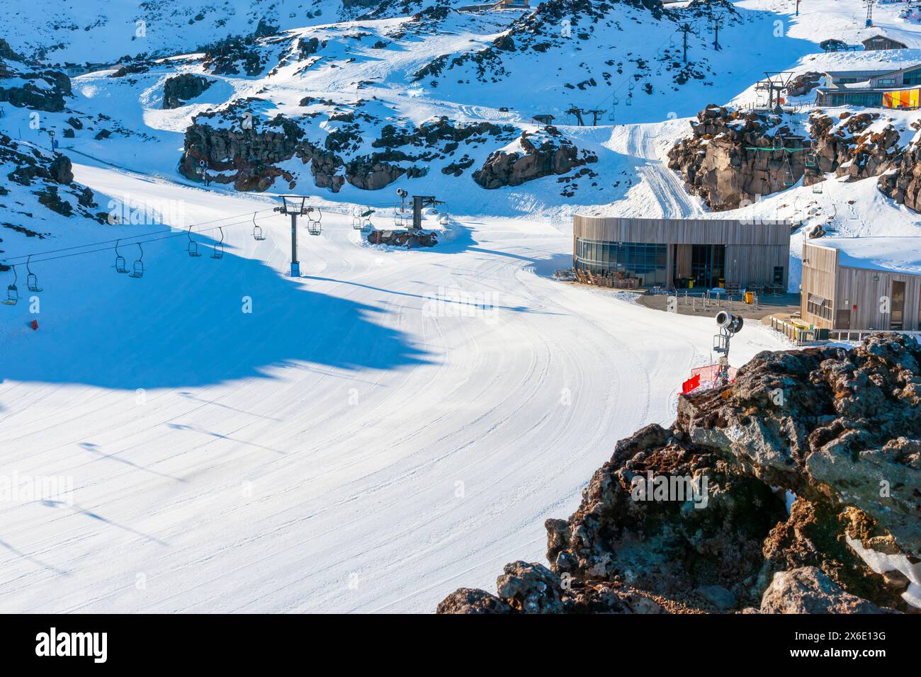 Whakapapa groomed ski-field and facilities buildings on shady side of mountain as sun rises on New Zealand Stock Photo