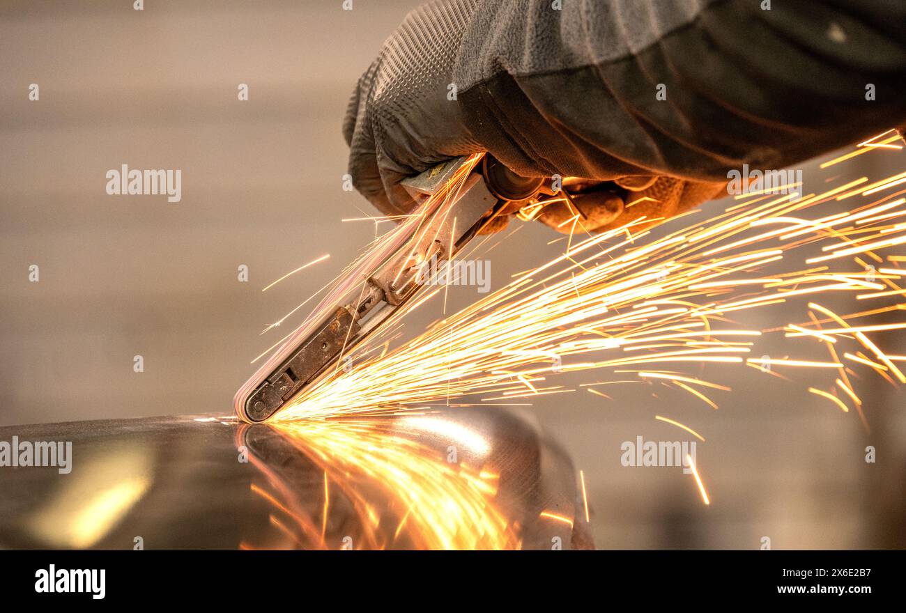 Close-up image of a worker using an angle grinder on metal, generating a bright spray of sparks in a workshop setting. Stock Photo