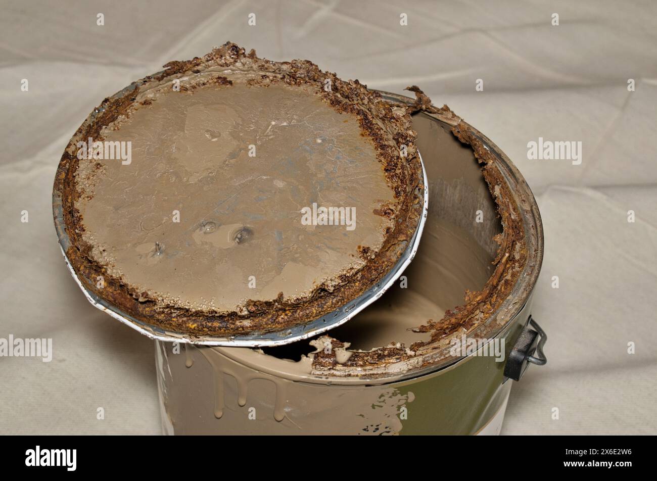Rusted old metal paint tin with open lid on drop cloth brown expired storage. Stock Photo